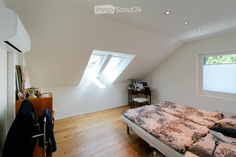 Bright attic bedroom with wooden flooring, slanted ceilings, large skylight windows, and a bed with patterned bedding.