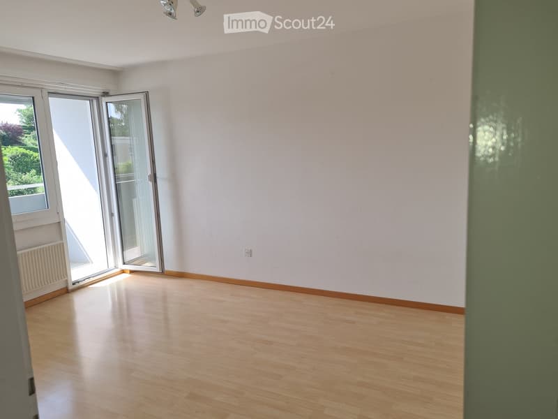 Empty room with light wooden flooring, white walls, and large sliding glass doors leading to a balcony.