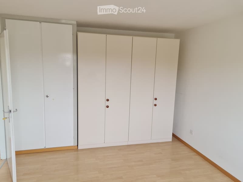 Empty room with light wooden flooring, white walls, and built-in white wardrobes with multiple doors.