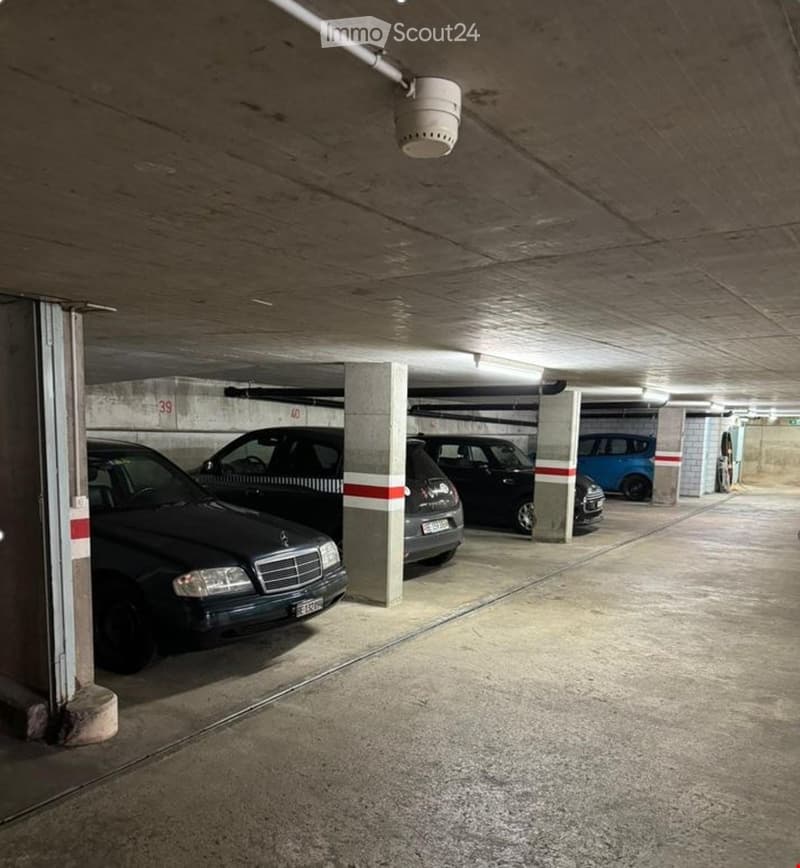 Underground parking area with several parked cars, concrete pillars, and numbered spaces.