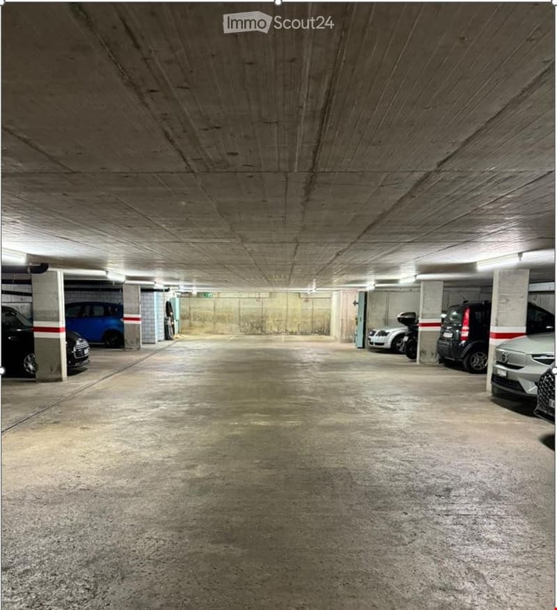 Underground parking area with several parked cars and a motorcycle, concrete floors and ceilings, and designated parking spaces.
