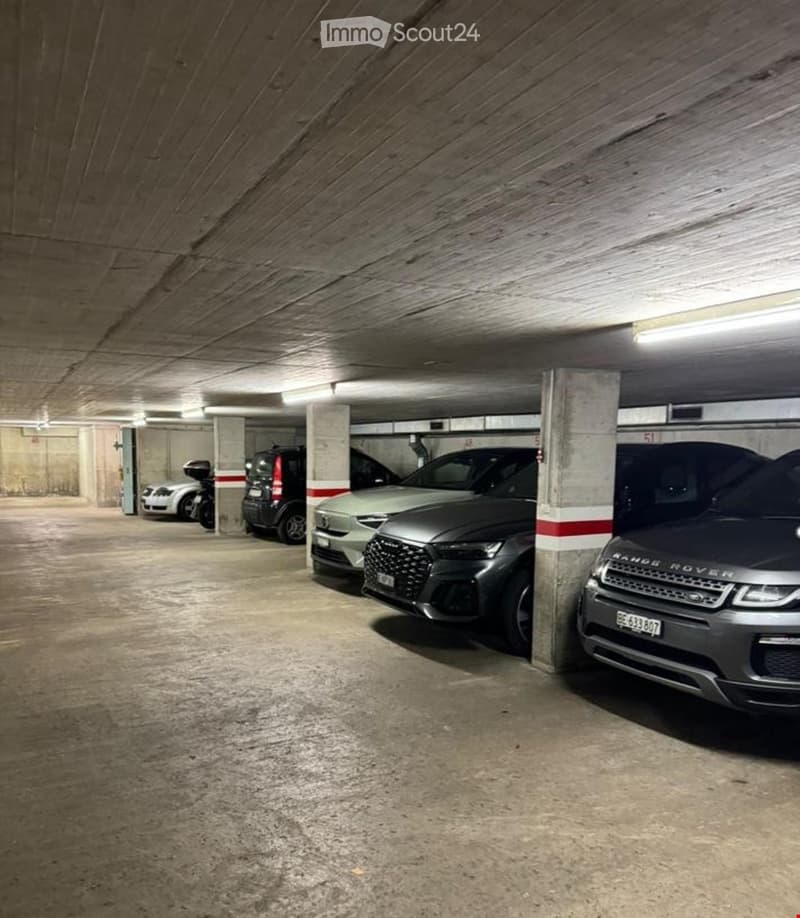 Underground parking area with several parked cars and a motorcycle, featuring concrete floors and pillars.