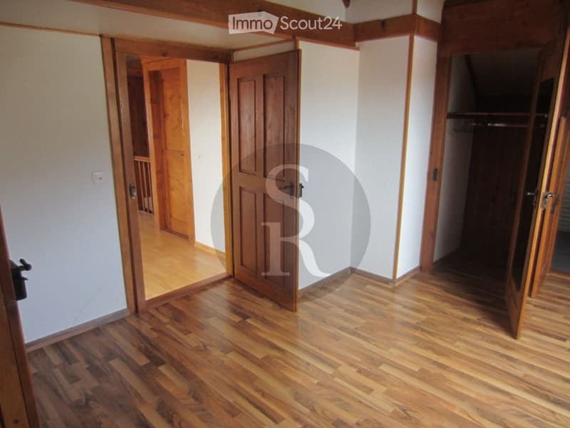 Empty room with wooden flooring and white walls, featuring multiple open wooden doors leading to other spaces.
