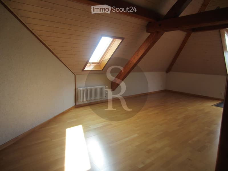 Empty attic room with wooden floors, exposed wooden beams, and a skylight window allowing natural light to enter.