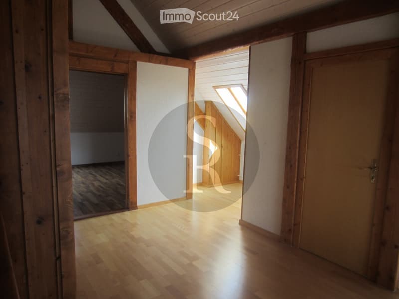 Empty hallway with wooden flooring, white walls, and exposed wooden beams. Natural light streams in from a skylight at the far end.