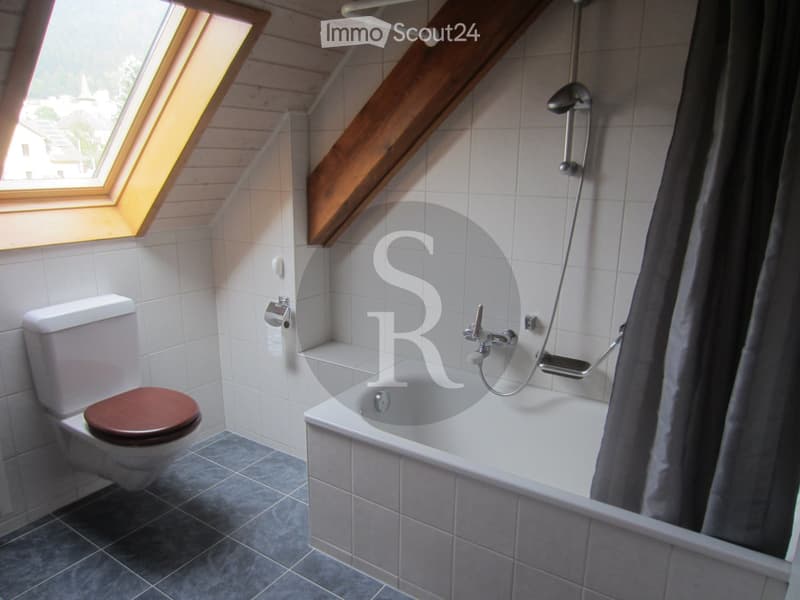 Bathroom with a toilet, bathtub, and shower, featuring a skylight window and wooden slanted ceiling beams.