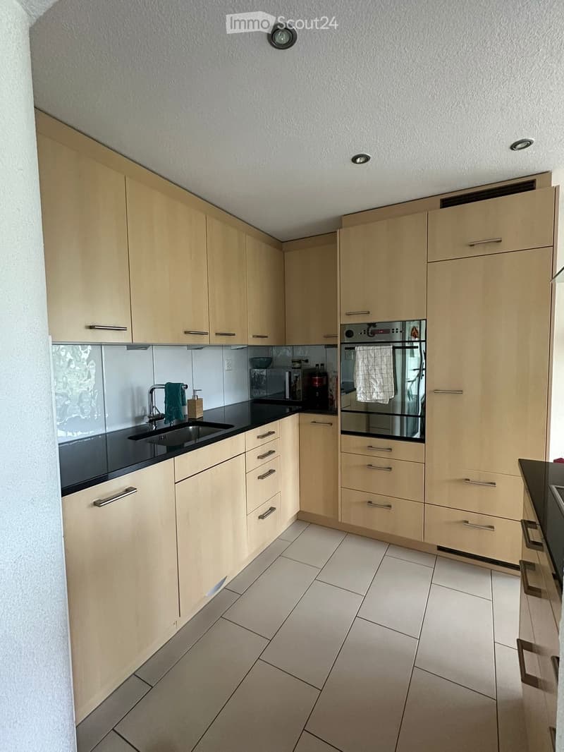 Modern kitchen with light wood cabinets, stainless steel appliances, and a black countertop.