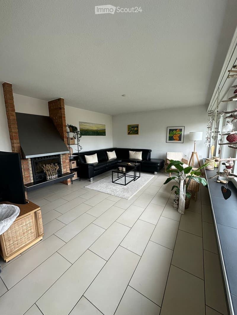 Modern living room with a black sectional sofa, coffee table, armchair, fireplace, and decorative plants.
