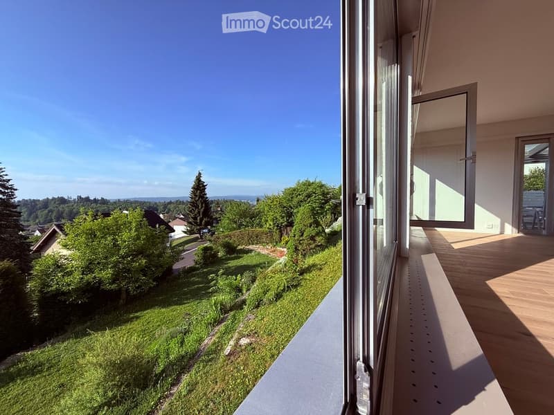 Balcony with wooden flooring, large sliding glass doors, overlooking a green garden and distant landscape.