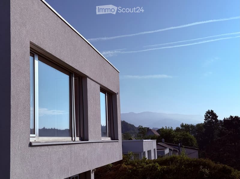 Modern building with large windows and a clean, minimalist design, set against a backdrop of mountains and trees.