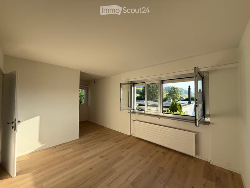 Empty room with wooden flooring, white walls, and large windows with open shutters, allowing natural light to fill the space.