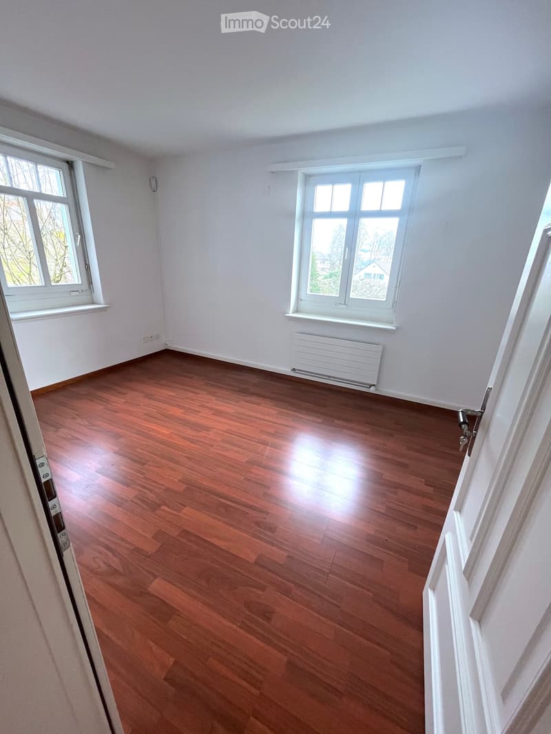 Empty room with wooden flooring, white walls, and large windows allowing natural light. No furniture or equipment is present.