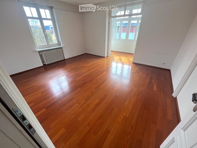 Empty room with wooden flooring, white walls, large windows, and a radiator under one window.
