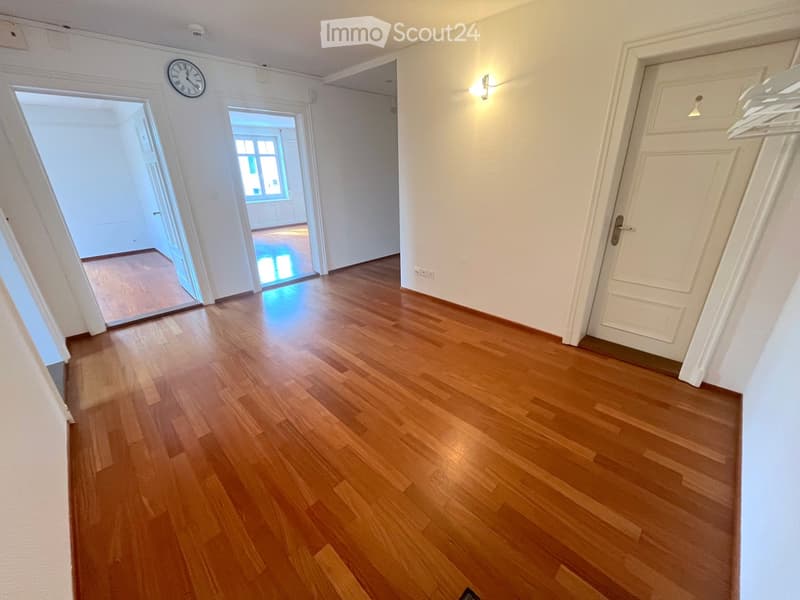 Empty hallway with wooden flooring, white walls, and several doors leading to other rooms.