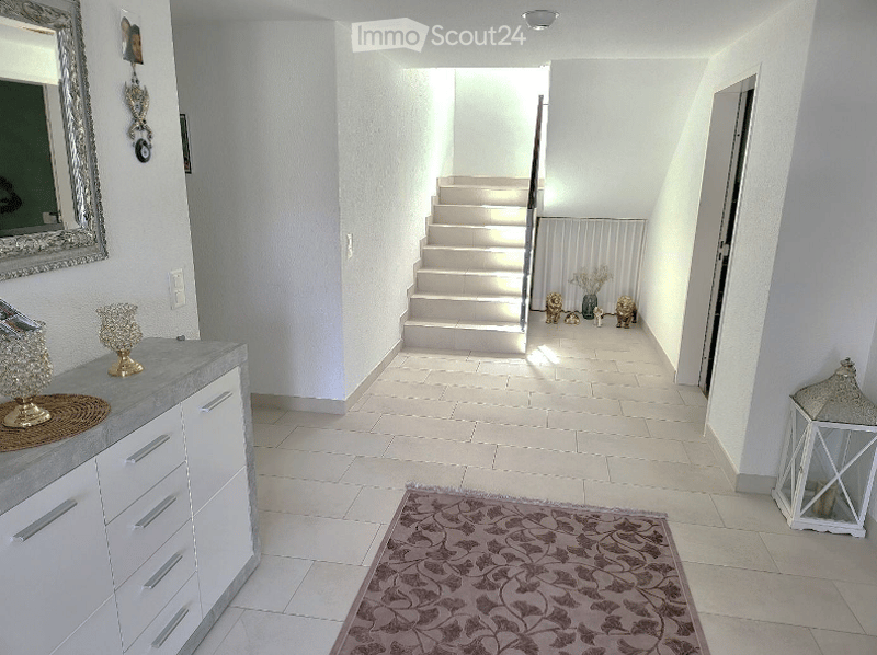 Entrance hall with white tiles, white cabinet, mirror, rug, staircase, and decorative items