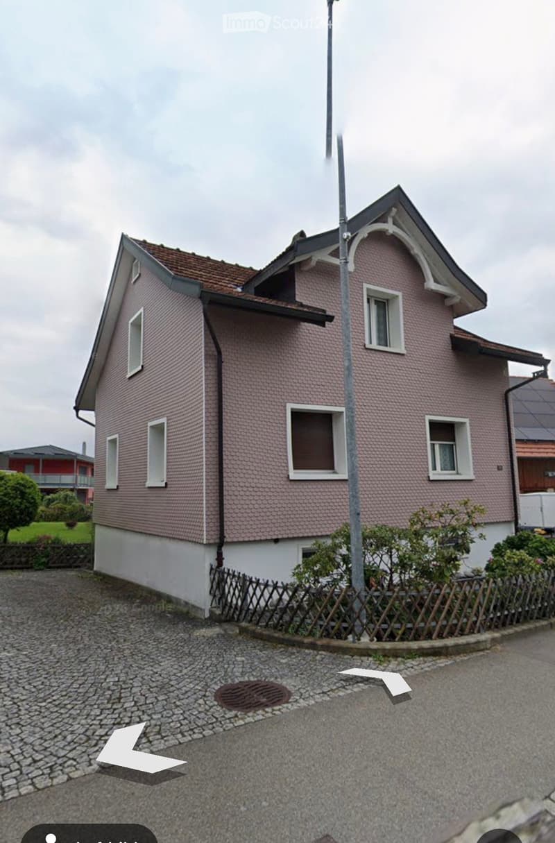 Two-story house with pink exterior, white trim, multiple windows, and a small garden area with a wooden fence.