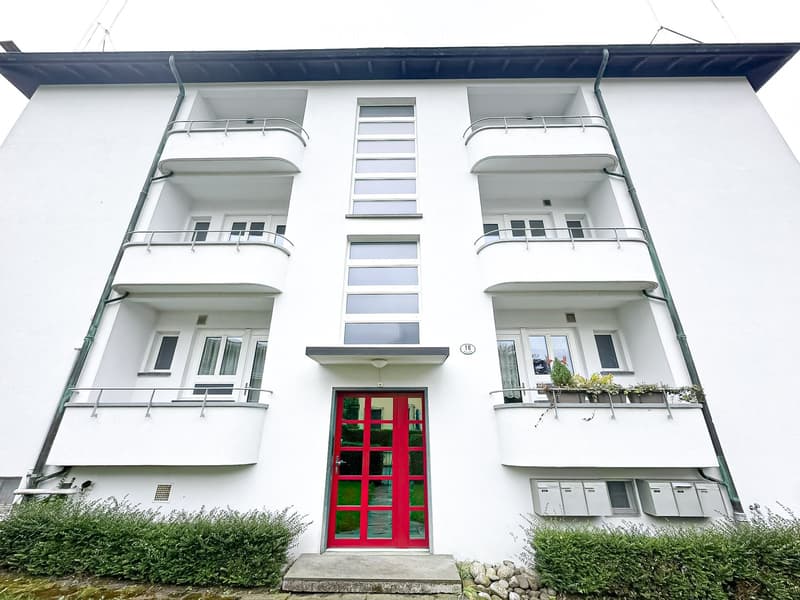 White multi-story building with balconies, large windows, and a red front door.