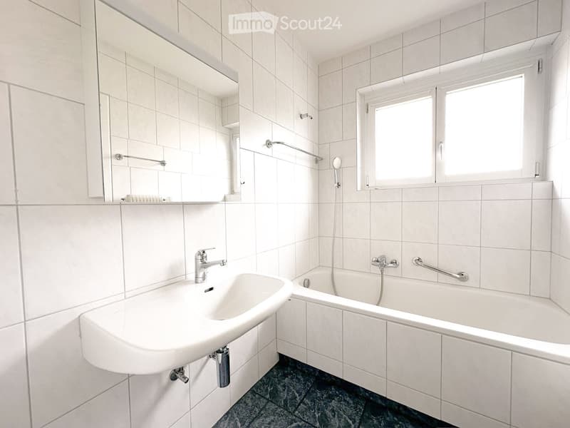 Modern bathroom with white tiles, a sink, a bathtub, and a large mirror above the sink.