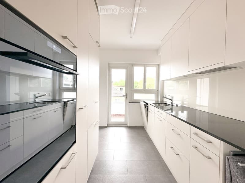 Modern kitchen with white cabinets, black countertops, stainless steel appliances, and ample natural light from windows and a door leading outside.