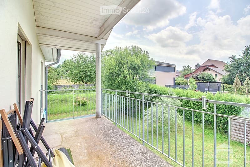 Balcony with metal railing, grassy area, view of trees and buildings in distance