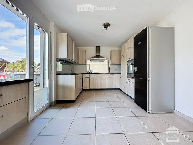Modern kitchen with light wooden cabinets, stainless steel appliances, and tiled flooring.