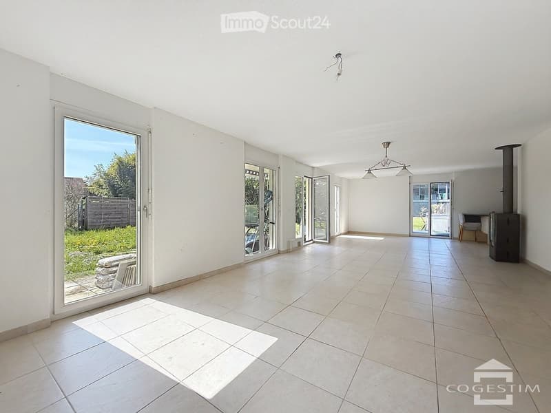Empty room with tiled floor, white walls, large windows, and a fireplace in the corner.