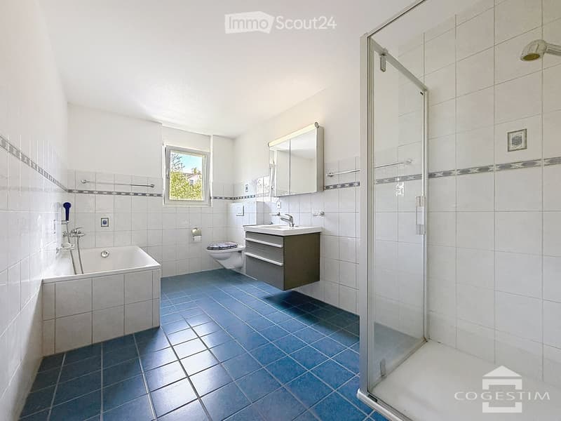 Modern bathroom with a bathtub, toilet, sink, mirror, and a glass-enclosed shower. Blue tiled floor and white tiled walls with decorative borders.