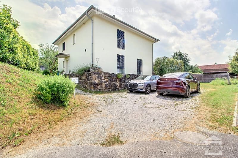 2 story house, white, 2 cars parked in front, paved driveway, stone wall, garden