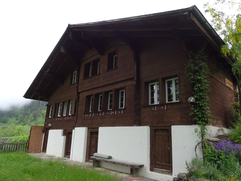 Traditional wooden house with white lower facade, multiple windows, and a bench in front.