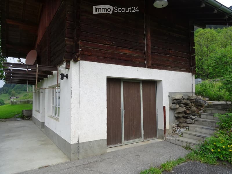 Two-story wooden house with white plaster walls, wooden doors, and a stone staircase leading up to the entrance.