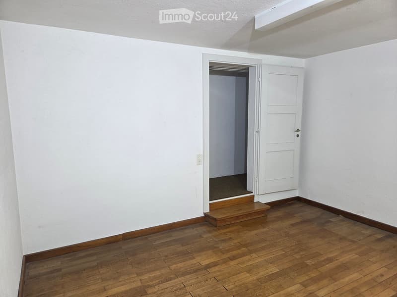 Empty room with wooden flooring, white walls, and a doorway leading to another space.