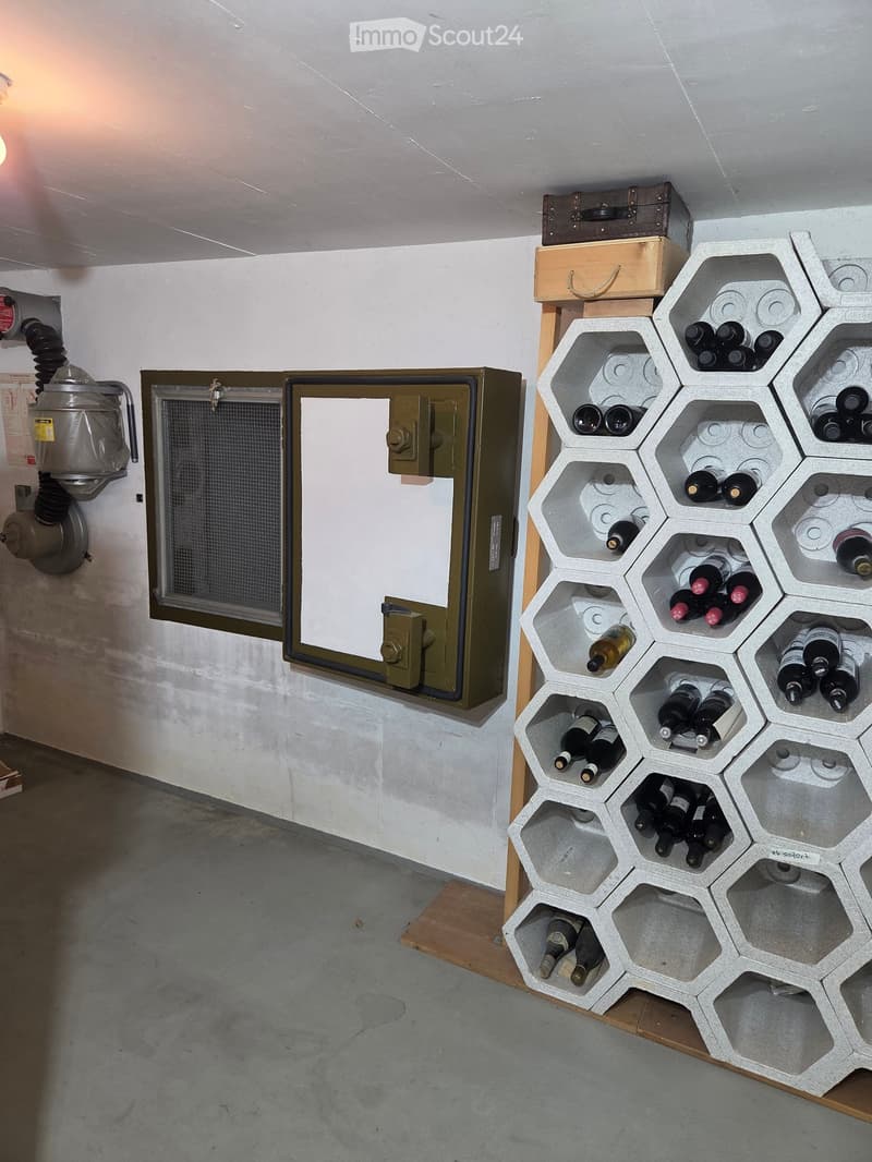 A room with a hexagonal wine rack filled with various wine bottles, a vent on the wall, and a small wooden box on top of the rack.