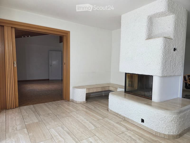 Modern living room with a large stone fireplace, tiled floor, and wooden door leading to another room.