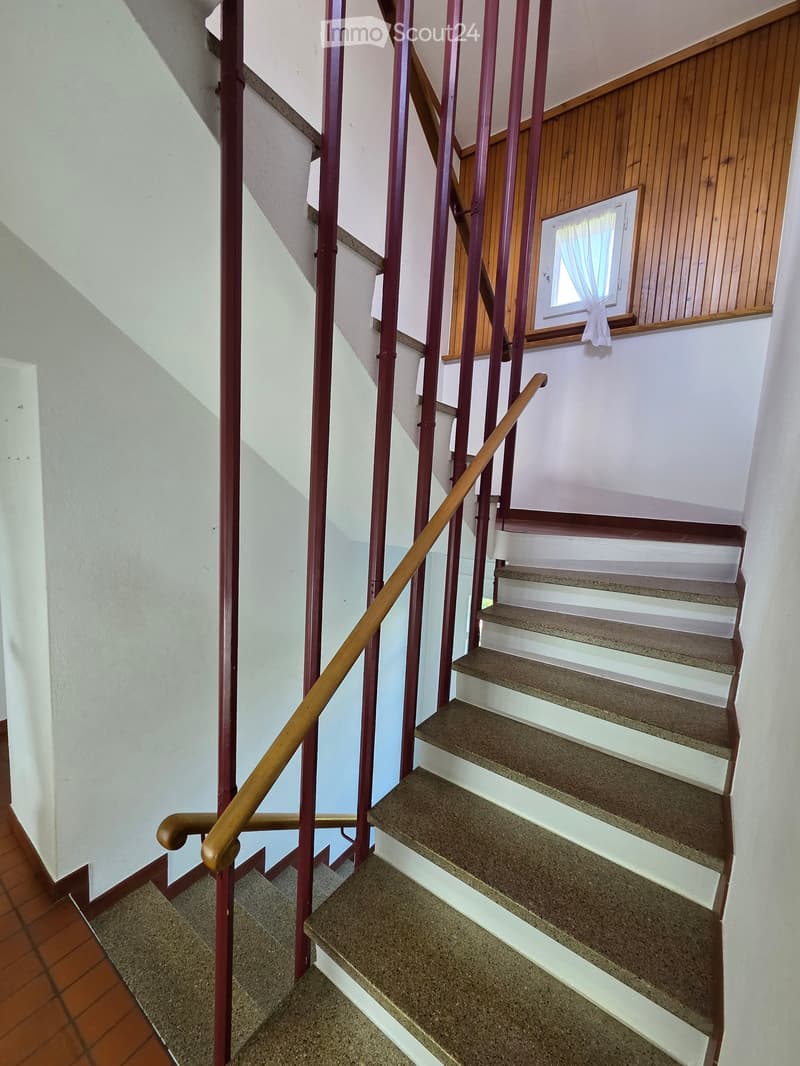 Staircase with red metal railings and wooden handrails, leading to an upper level with a window and wooden paneling.