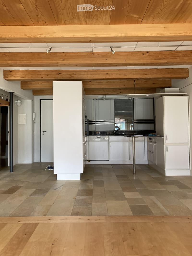 Modern kitchen with white cabinets, stainless steel appliances, and a central island. Exposed wooden beams on the ceiling and a mix of tiled and wooden flooring.