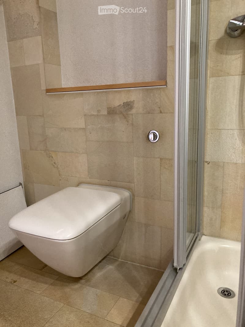 Modern bathroom with beige tiled walls and floor, featuring a white toilet and a glass-enclosed shower area.