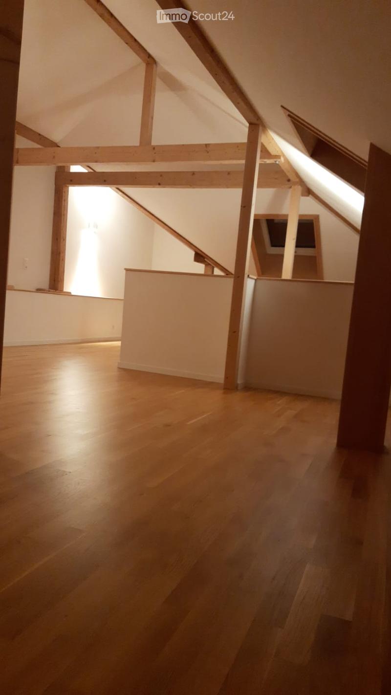 An empty attic space with wooden beams, exposed wooden floor, and natural light coming through skylights. No furniture or furnishings are present.