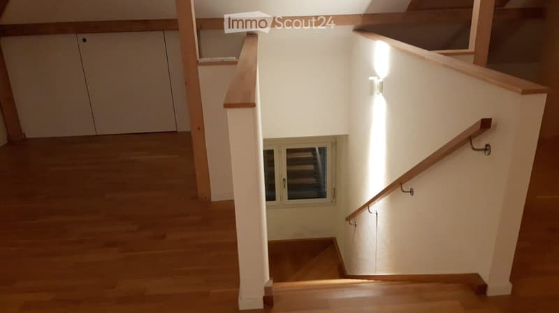 Spacious hallway with wooden flooring, white walls, and a staircase leading upwards, featuring wooden railings and built-in lighting.