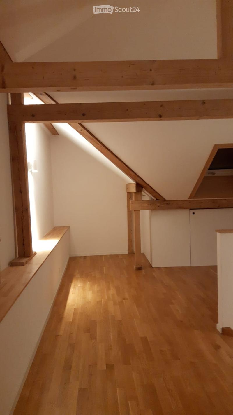 Empty attic space with wooden beams, exposed wooden floor, and natural light from skylights and side windows.
