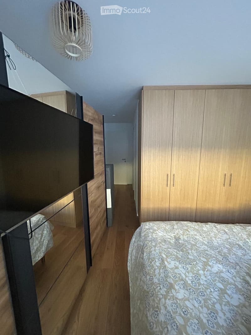 Bedroom with wooden floor, bed with floral duvet, large wardrobe, and a fan on the ceiling.