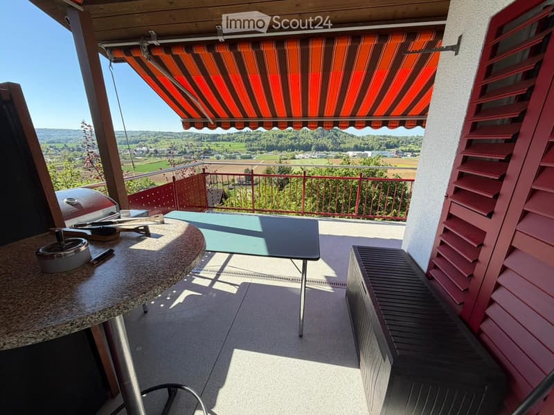 Balcony with a table, bench, grill, and scenic countryside view.