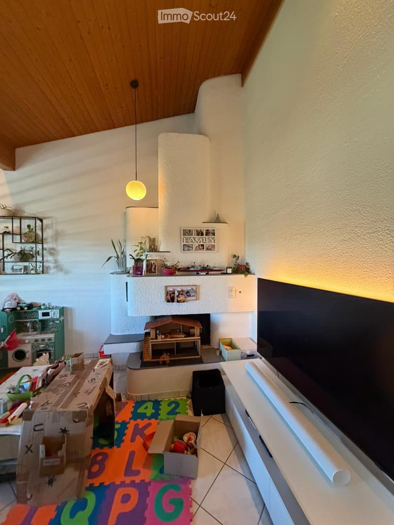 Cozy living room with a fireplace, colorful play mat, TV, and various toys and decorations.