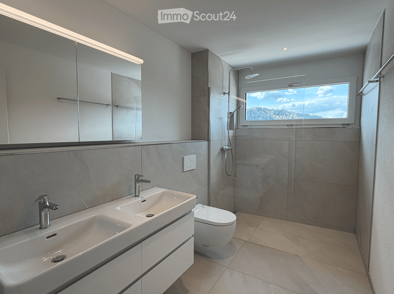 Bathroom. Modern bathroom with double sink, toilet, large mirror, and shower area with a window offering a scenic view.