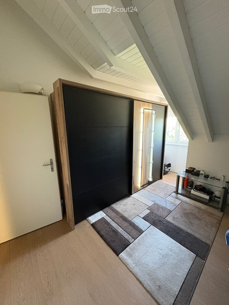 Attic hallway with wooden flooring, grey tiled area, and a black door leading to another room.