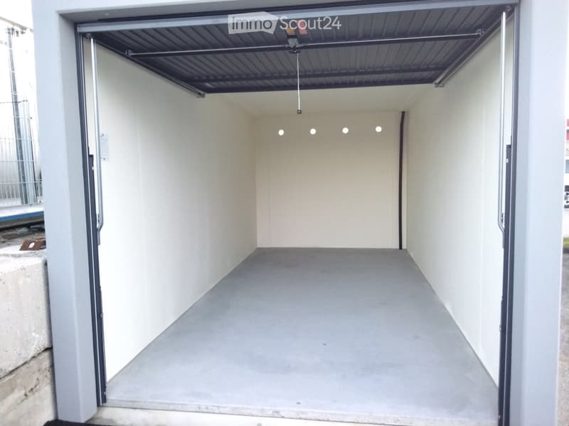 Open garage with concrete floor, white walls, and a metal ceiling with lighting fixtures.