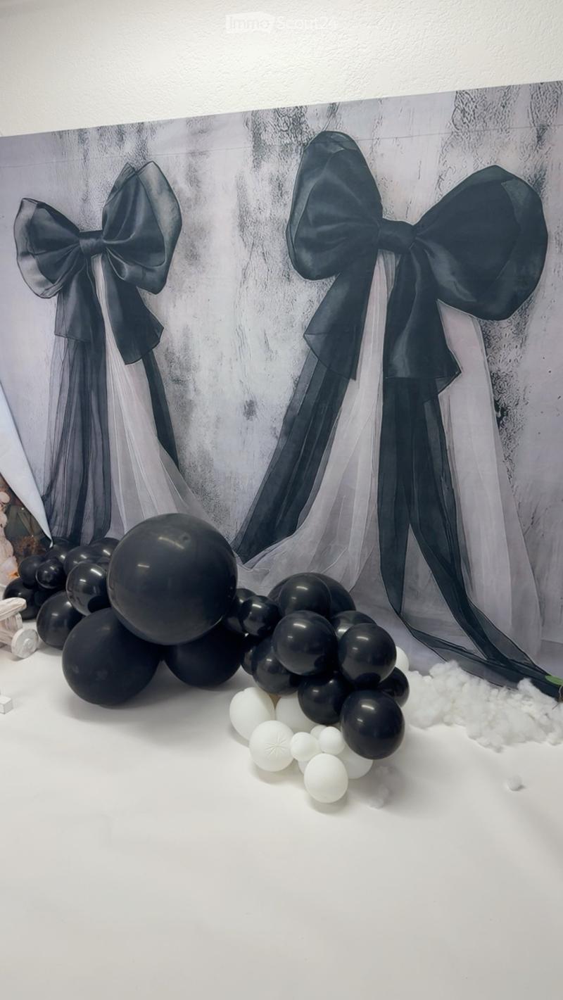 A decorative display featuring black and white balloons arranged in clusters, with large black bows and a sheer fabric backdrop.