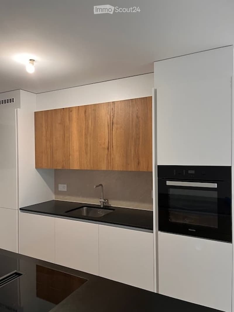 Modern kitchen with white and wooden cabinets, black countertops, and built-in oven.