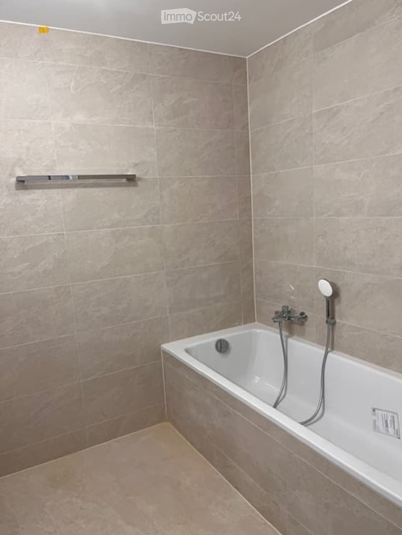 Modern bathroom with a white bathtub, tiled walls, and a built-in showerhead and faucet.