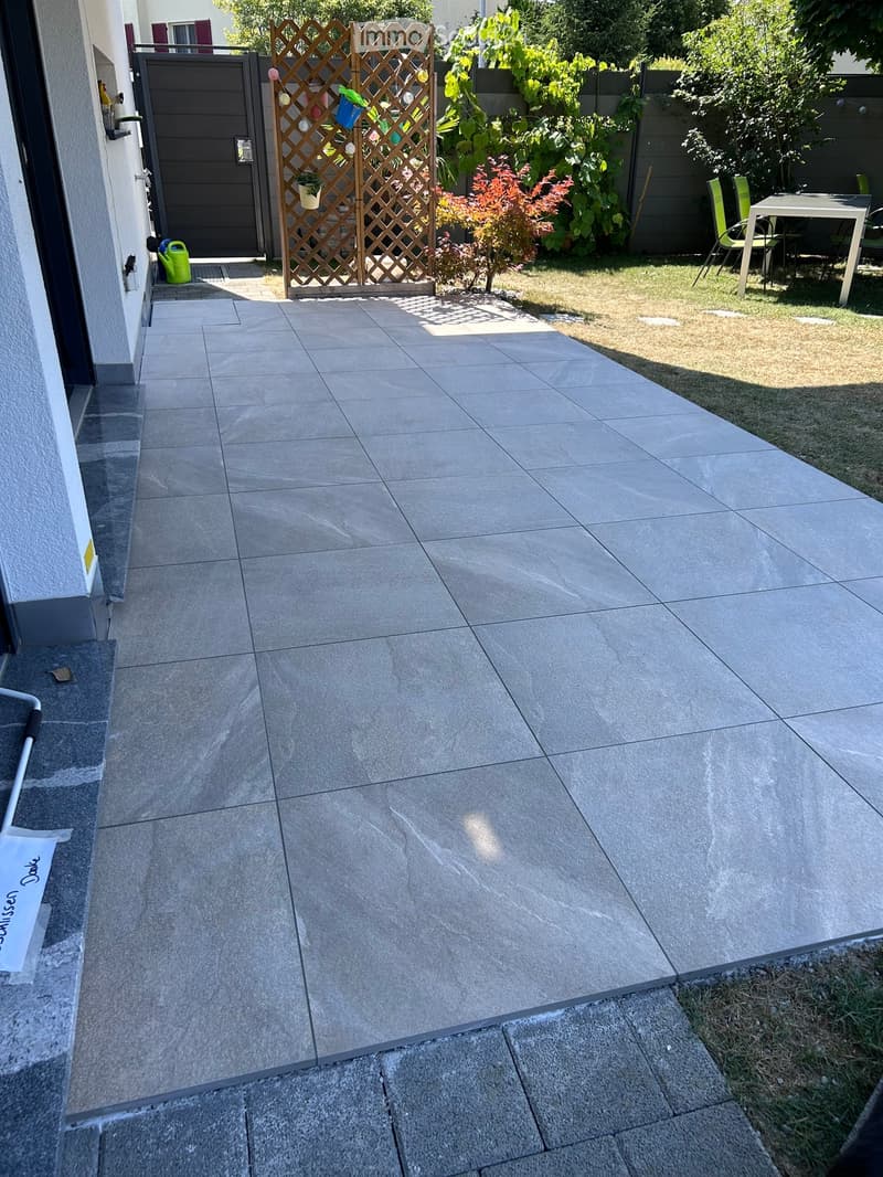 Patio area with tiled flooring, small garden with plants, a wooden lattice structure, and outdoor furniture including a table and chairs.