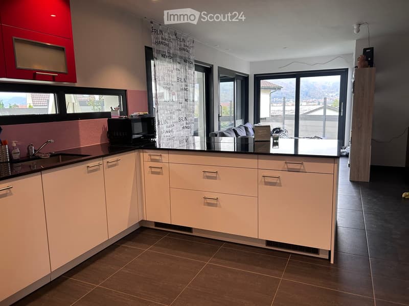 Modern kitchen with light-colored cabinets, black countertop, and stainless steel sink. Large windows offer a scenic view.